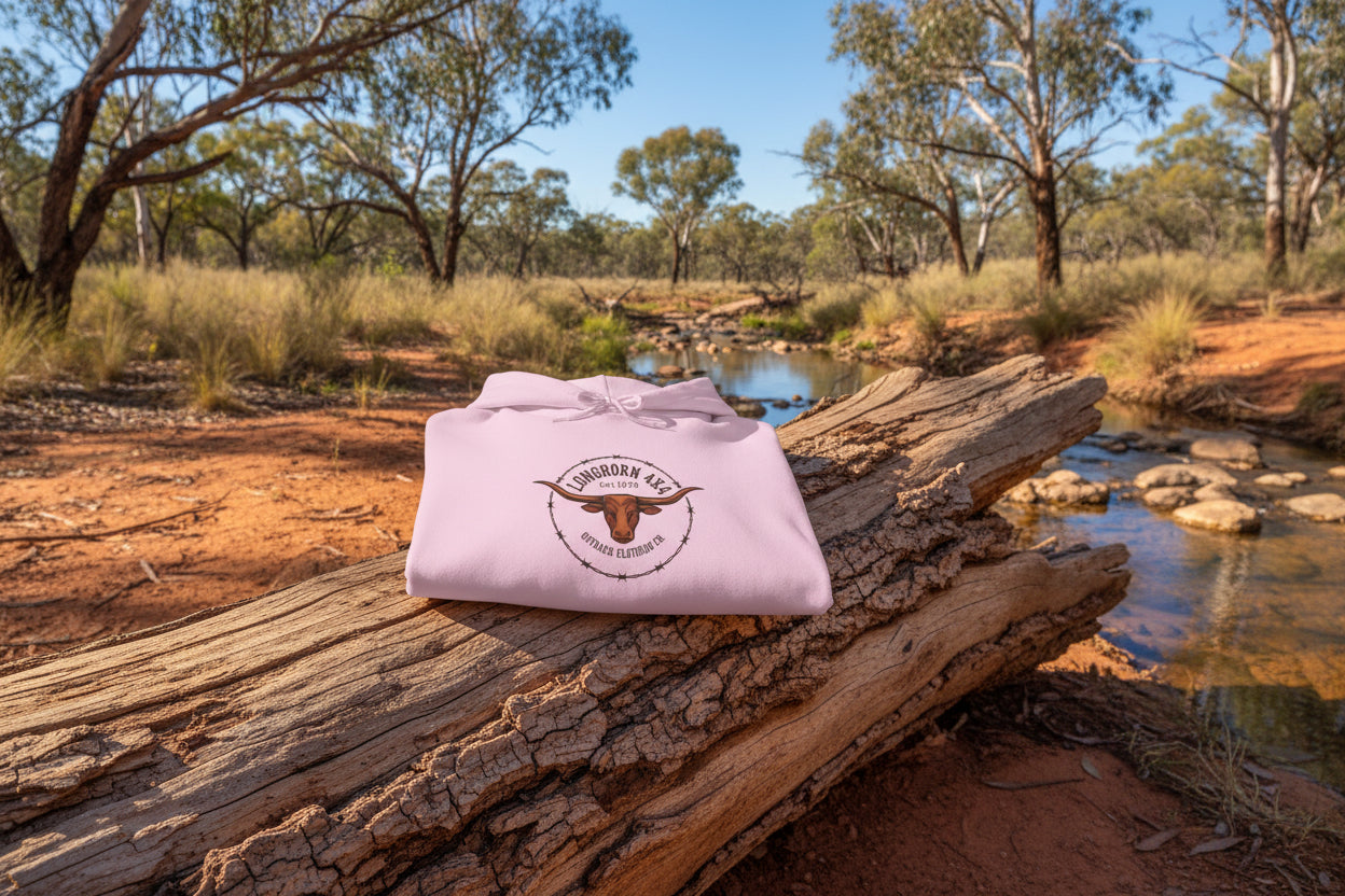 Pink hoodie with a longhorn logo on a rustic log by a creek in the Australian outback.