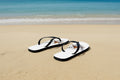 White flip-flops with a logo on the straps against a Sandy and ocean background