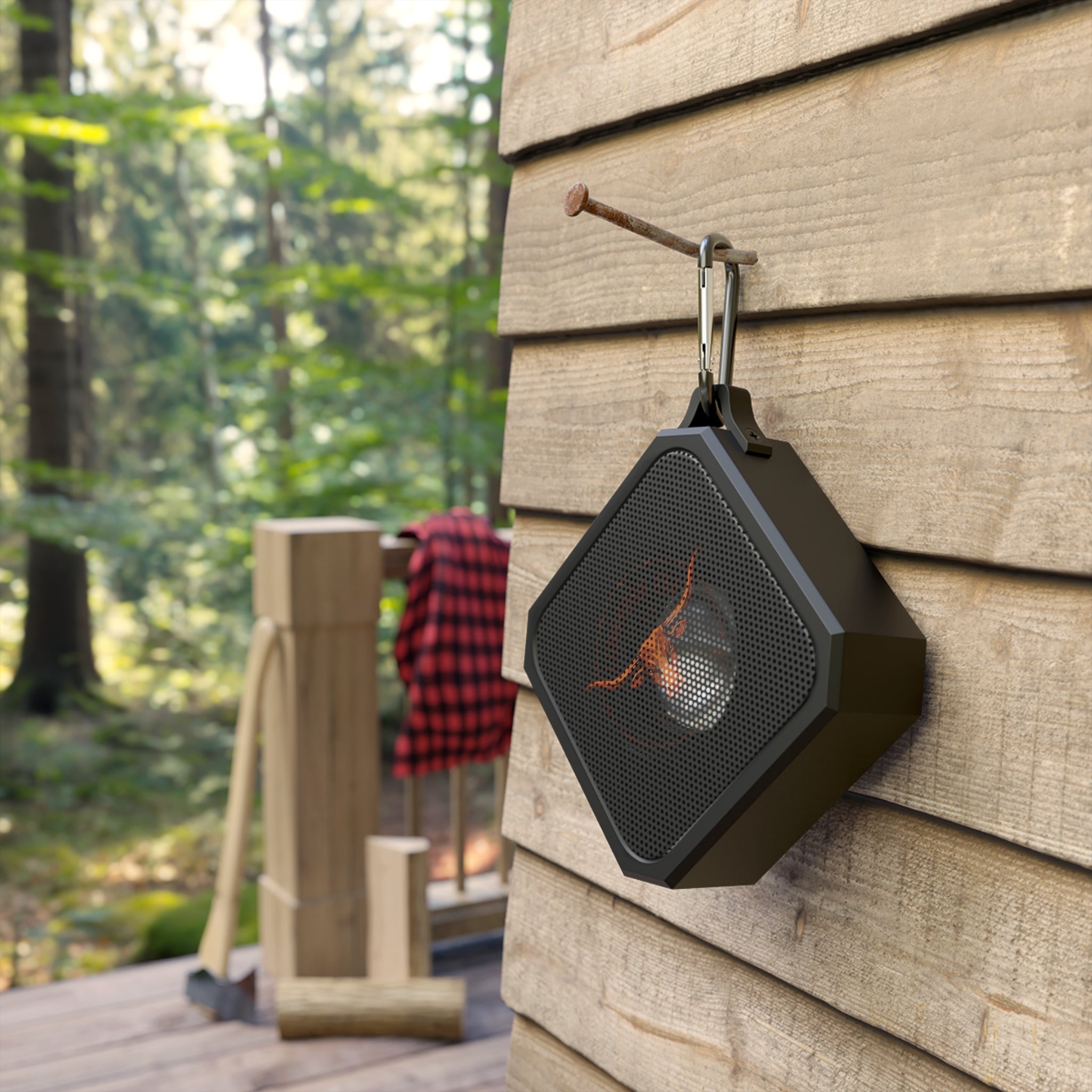 Black portable speaker hanging on a wooden wall with a forest background