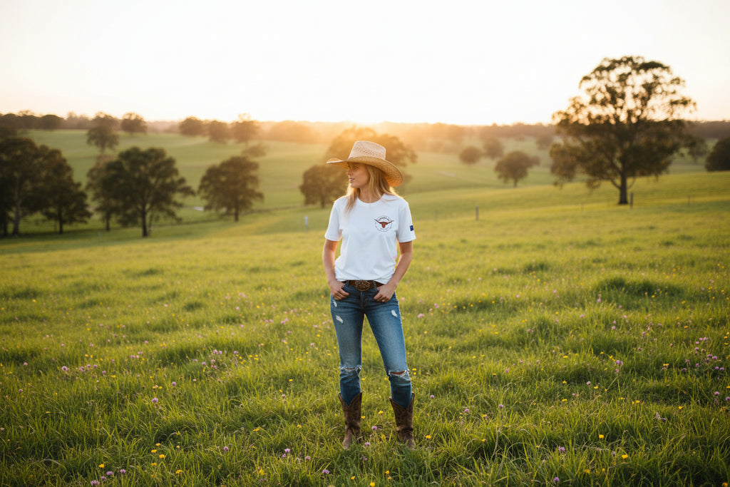 White t-shirt with a logo on the chest with a cow girl standing in a green pasture background