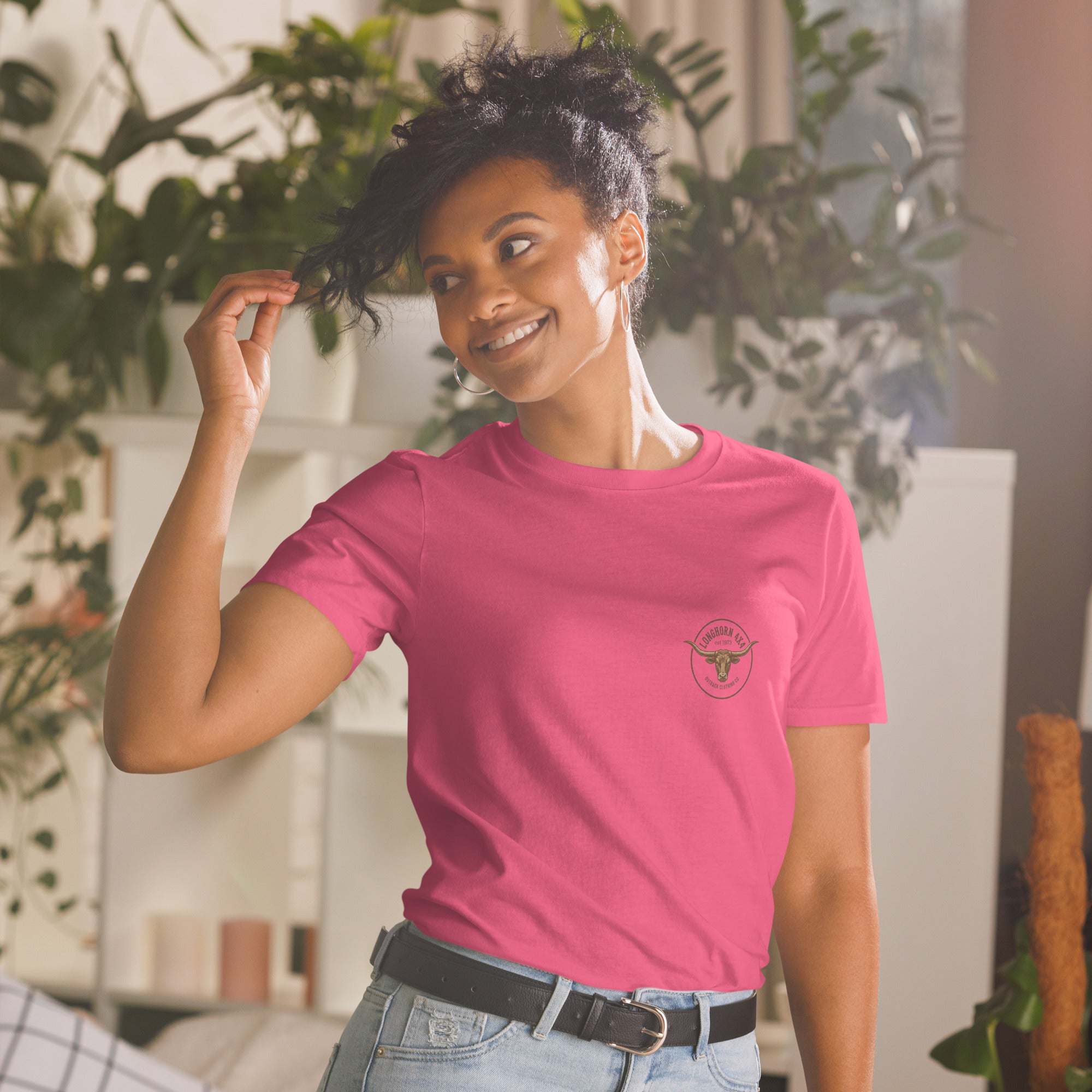 Girl Playing with her hair, wearing a pink longhorn 4x4 t-shirt with plants in the background. 