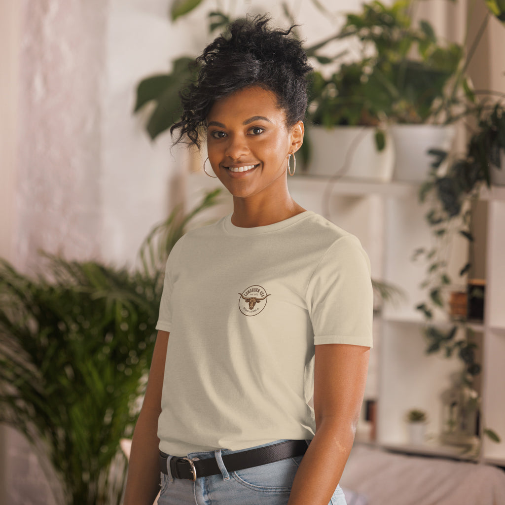 Woman wearing a light-colored t-shirt with a logo, standing in a room with plants.